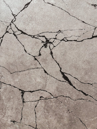 Intricate cracks weave across a weathered concrete surface, creating a fascinating display of...