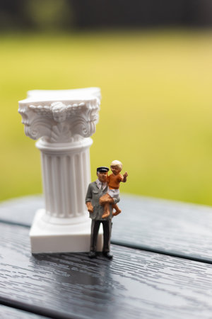 A grandfather carries a little child boy, with a miniature column beside them. A figurine of a grandpa and his grandson walking outside. Different generations enjoy time together. Family time.の写真素材