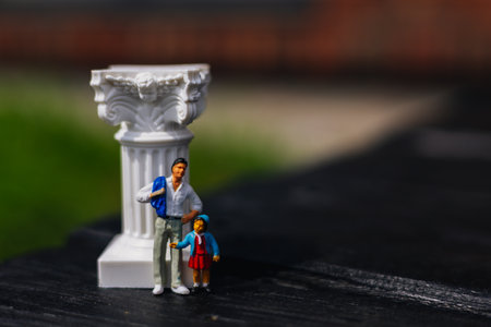 A miniature father and daughter stand beside a decorative pillar outdoors. The figures of a dad and kid stand near a column, creating a charming scene. Family weekends. Single parent and a child.の写真素材