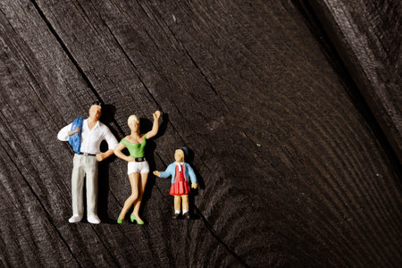 Miniature family figurines stand on a textured wooden surface, enjoying the warm sunlight. The figurines of father, mother and a little girl. They stand together and the woman waves with her hand.の写真素材