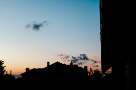 The silhouette of a house at dusk, under a colorful, cloud-filled sky at twilight. A silhouetted house at dusk with clouds against a gradient sky, capturing the tranquil ambiance of twilight.の写真素材