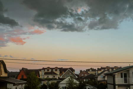 Storm clouds gather over a suburban neighborhood at sunset, creating a dramatic scene. Dramatic sky with dark storm clouds gathering over a residential area. A beautiful, yet ominous, weather scene.の写真素材