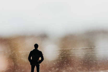 A man standing with his back facing us, gazing out of a window and lost in thought. A silhouette of a business person stands looking out a window. The blurred background adds a sense of mystery.の写真素材