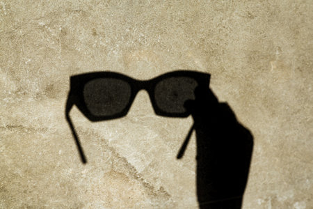 The shadow of sunglasses, cast on a textured wall, creates a unique and stylish image. A shadow of sunglasses is cast on a textured surface, showing a creative and artistic composition.の写真素材
