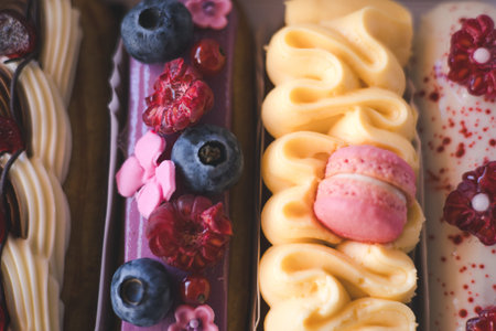 Delicious eclairs with fresh berries and macarons beautifully displayed in a bakery box. A close-up...