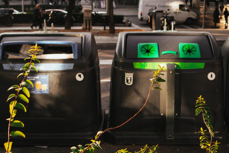 Two large black recycling bins stand on a city street, ready for waste disposal. A pair of trash...