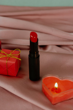 Romantic still life of red lipstick, a heart candle, wrapped present A romantic still life featuring lipstick, a heart-shaped candle, and a wrapped gift on a satin surface, perfect for Valentine's Dayの写真素材