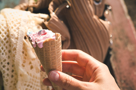 Hand holding a melting pink ice cream cone on a sunny day, perfect for summer. A close-up shot...