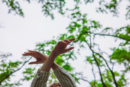 Arms crossed with open hands reaching towards the sky through the trees. A person's gently crossed...