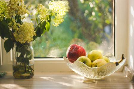 Sunlit still life featuring fresh fruit and flowers on a windowsill. A still life captures a sunlit...