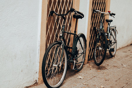 Two vintage bicycles lean against a textured wall and ornate metal grate. The bikes have a classic design and the scene has nostalgic aesthetic. Urban lifestyle, eco transport and sustainable living.の写真素材