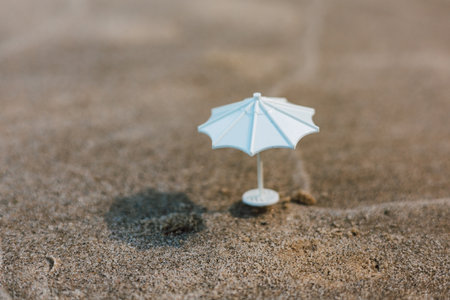 A miniature white parasol sits on textured sand, creating a simple yet captivating scene. A miniature white parasol stands on a sandy surface, possibly a beach or desert suggesting a small-scale sceneの写真素材