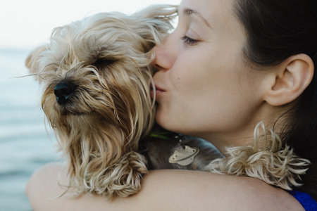 Tender portrait of young woman hugging and kissing small Yorkshire terrier dog. Authentic emotional moment showing love, care, friendship and human animal bond. Perfect for lifestyle and pet themes.の写真素材