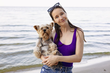 Happy young woman in swimsuit holding small dog at the beach. Authentic summer portrait with real...