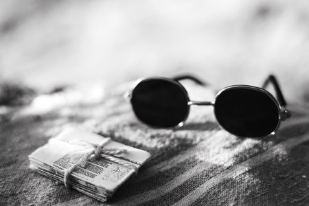 Vintage sunglasses and a stack of papers on a striped surface. Black and white photograph showcases a pair of round sunglasses next to a bundled stack of newspapers tied with twine. A nostalgic feel.の写真素材