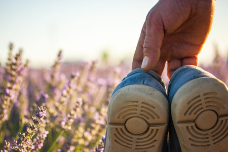 Shoes held above lavender field. An hand holds the heels of blue aged shoes over a soft focus...