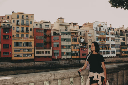 Young woman standing on a bridge in Girona, Spain. Editorial image with colorful residential...
