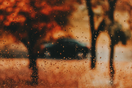Moody autumn scene through a rainy window â€“ raindrops on wet glass, blurred trees in warm...