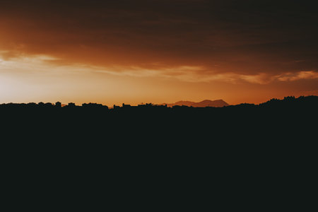 Sunset silhouette over mountains and cityscape. A stunning sunset paints the orange sky with warm...