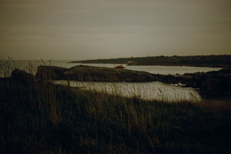 Coastal landscape with a small red-roofed building on a rocky island. A serene coastal scene captures a tranquil moment with a small building nestled on a rocky island, under a cloudy sky.の写真素材