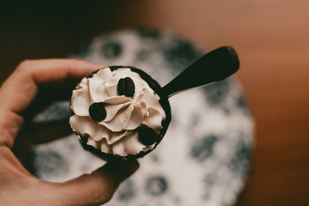 Delicious coffee dessert with whipped cream and coffee beans, close-up shot. A hand holds a small dessert cup filled with whipped creamy filling ready to be enjoyed and eaten. Dark key moody food.の写真素材