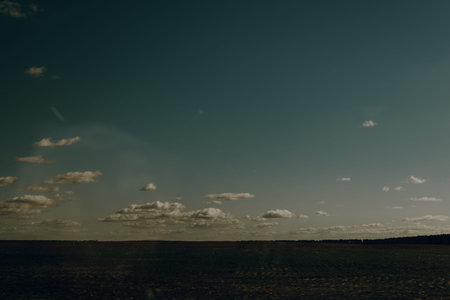 Dramatic sky over a cultivated field on a sunny day with scattered clouds. This image captures a...