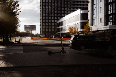 KYIV, Ukraine 25 October 2025. Modern city street scene with electric scooter, buildings, and overcast sky. An electric scooter sits on a brick sidewalk in front of a modern building, a car parked.のeditorial素材