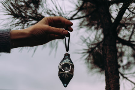 Female hand holding a vintage blue Christmas ornament against a cloudy sky. A hand delicately suspends a beautiful, antique glass Christmas bauble, evoking a sense of nostalgia and holiday cheer.の写真素材