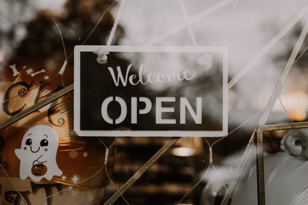 A shop sign for Halloween with text 'Welcome, open' on black plate. A shop window displays a welcome...