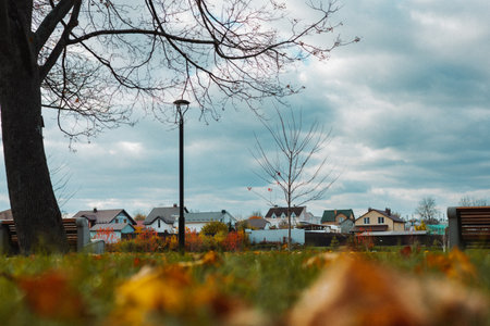 Autumn landscape with houses, trees, and cloudy sky in a residential area. A serene autumnal scene captures the essence of a peaceful neighborhood under a dramatic sky Suburban parkland in fall seasonの写真素材