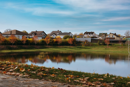 Kyiv Oblast, Ukraine. November 1, 2025 Autumn landscape with houses by the lake under blue sky in sunny day. Autumnal pond reflecting colorful trees.のeditorial素材