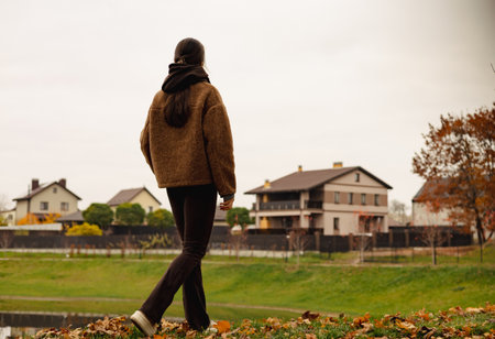 Stylish young woman walking outdoors in autumn park with smartphone, cozy brown outfit, calm mindful lifestyle, slow living and digital minimalism concept. Digital balance and slow living outdoor.の写真素材