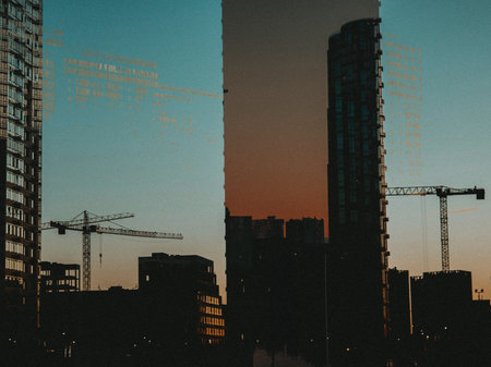 Cityscape at dusk with construction cranes and modern architecture. The silhouettes of buildings and cranes are set against a colorful sky, creating a dramatic urban scene. Grainy texture photo effectの写真素材