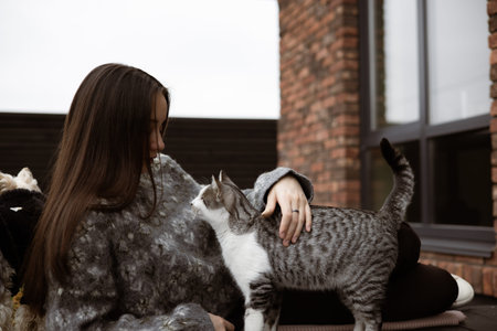 Warm autumn moment with a young woman sitting outside brick house, playing with a cat while enjoying...