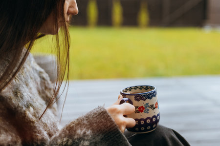 Cozy lifestyle moment of a woman holding a patterned ceramic mug and relaxing outdoors. A perfect scene for themes of slow living, mindfulness, comfort, relaxation, morning routine and hygge lifestyleの写真素材