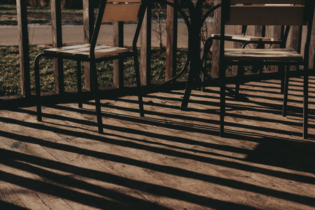 Wooden deck with chairs and table casting long shadows in the sunlight. The warm sunlight creates...