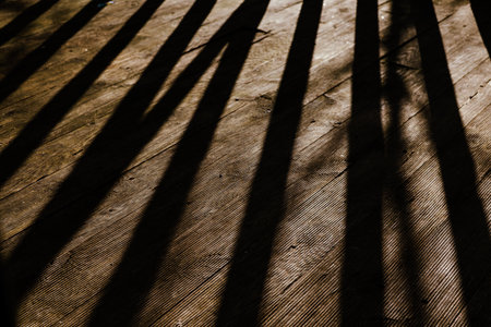Dramatic contrast long shadows cast across a weathered wooden deck in natural sunlight. The strong contrasts of light and shadow creates an interesting abstract pattern on aged wood terrace surface.の写真素材