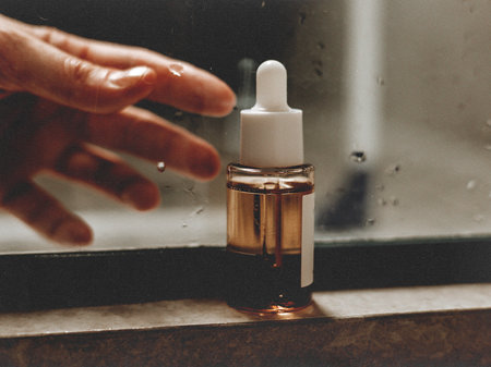 A digital art shot of a skincare serum bottle in a bathroom, a hand reaching towards it and water droplets on the glass, enhanced with textured overlays and film grain for a modern editorial aesthetic.の写真素材