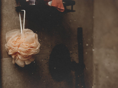 Soft bath sponge hanging in a shower with water droplets on a glass. A peach-colored bath sponge hangs in a shower, with water droplets on the glass. Modern bathroom interior. Spa day, daily routine.の写真素材