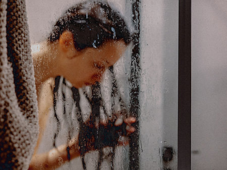 Woman in shower behind glass with water droplets, spa and wellness concept. A white woman is seen behind a glass shower door, creating a sense of privacy and relaxation.の写真素材