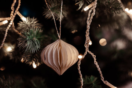 Elegant handmade paper ornament hanging on a Christmas tree with warm fairy lights and festive bokeh. Minimalist holiday decor capturing cozy New Year 2026 ambience and modern seasonal aesthetic.の写真素材