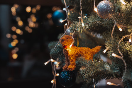 Cozy Christmas tree ornament with a handmade plush dog, glowing fairy lights and warm festive bokeh. Perfect for New Year 2026 ambience, holiday decor concepts, seasonal celebration design projects.の写真素材