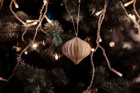 Elegant handmade paper ornament hanging on a Christmas tree with warm fairy lights and festive bokeh. Minimalist holiday decor capturing cozy New Year 2026 ambience and modern seasonal aesthetic.の写真素材