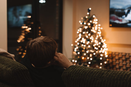 Cozy Christmas night scene at home with a person relaxing on a sofa, warm ambient lighting, and a beautifully decorated Christmas tree glowing with fairy lights, creating a peaceful festive atmosphereの写真素材