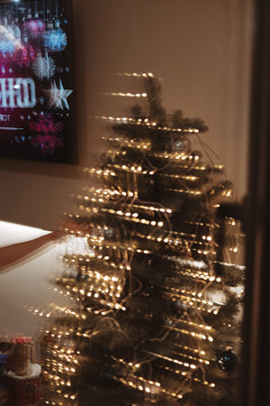 Moody, cinematic photo of a woman's reflection decorating a Christmas tree with lights and...
