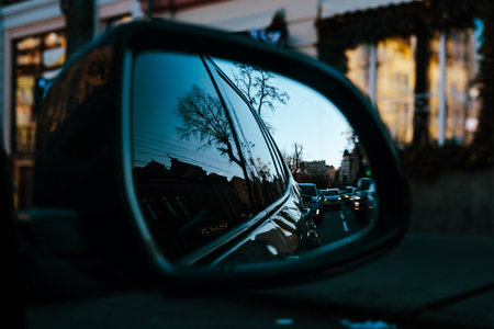 Reflection of a busy city street with traffic and classic architecture in a car side mirror, symbolizing commuting, journey, and city life. Urban travel perspective. Rear view mirror. Automobile trip.の写真素材
