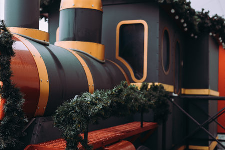 Decorative Christmas steam train decorated with pine garlands and lights at a holiday market. Festive winter background with gold and dark green colors. Ideal for seasonal advertising and promotion.の写真素材