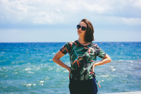 Young woman in a floral shirt posing on a sunny beach with blue sea background. Moody vintage film...