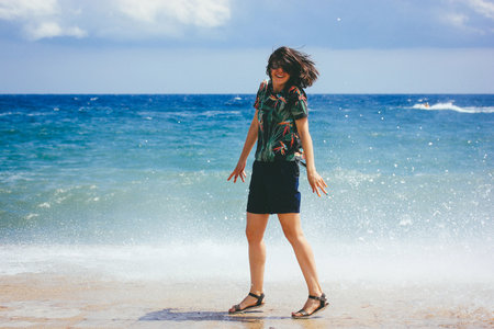 A happy young white woman jumping on sunny beach with blue sea background. Moody vintage film style...
