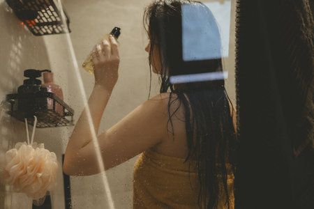 A candid, cinematic shot of a woman with wet hair wrapped in a yellow towel, standing in a bathroom....